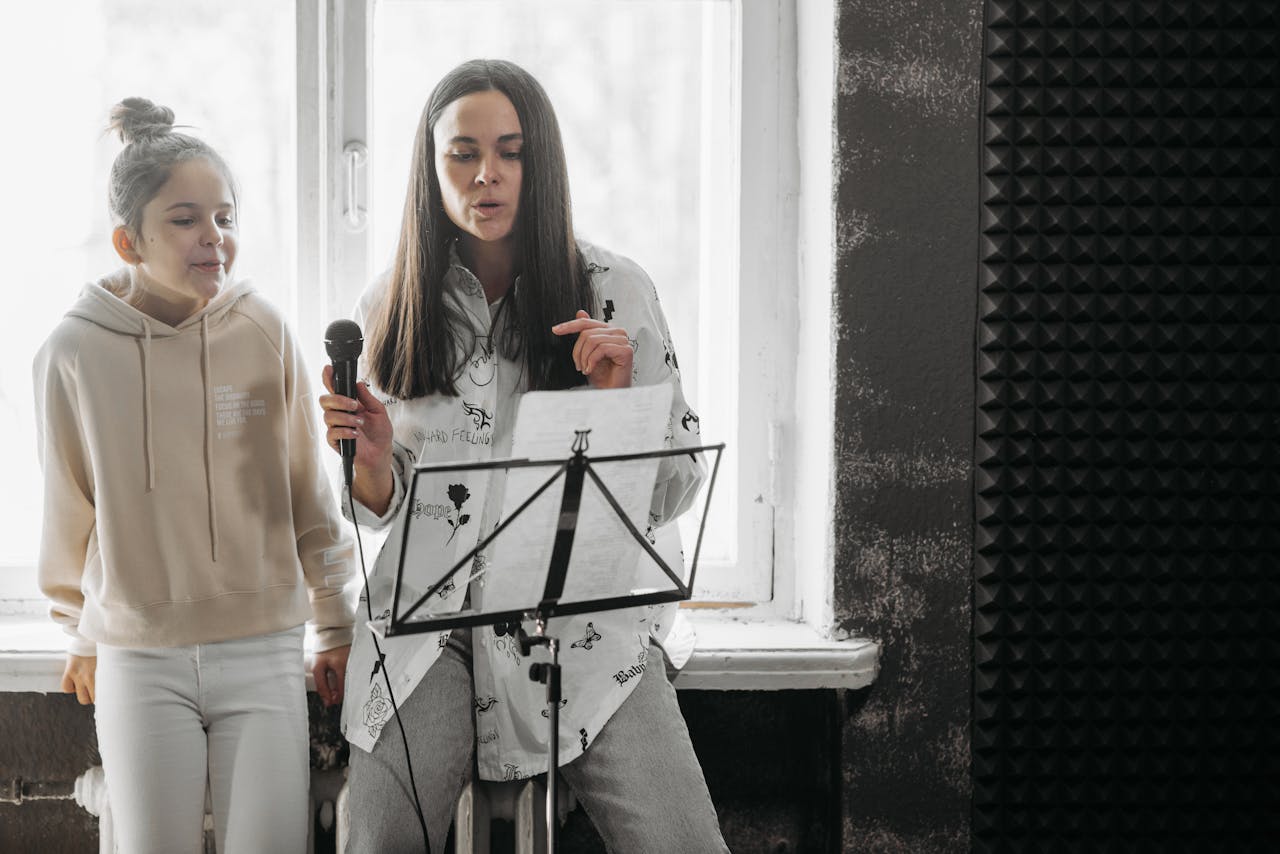 A woman and girl sharing a music lesson, singing with a microphone indoors.